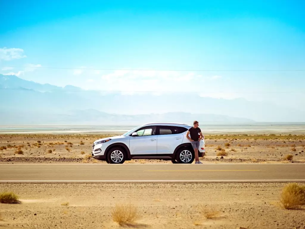 man standing beside white SUV near concrete road under blue sky at daytime